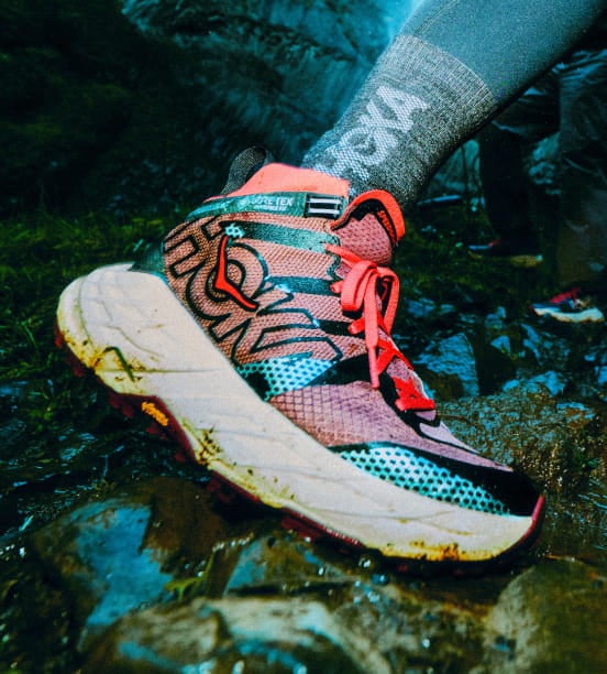 Gros plan d’une personne mettant les pieds dans l’eau rocheuse en portant des chaussures HOKA.